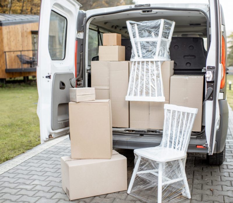Van vehicle trunk full of boxes and furniture near a house outdoors. Concept of moving to a new home and delivery