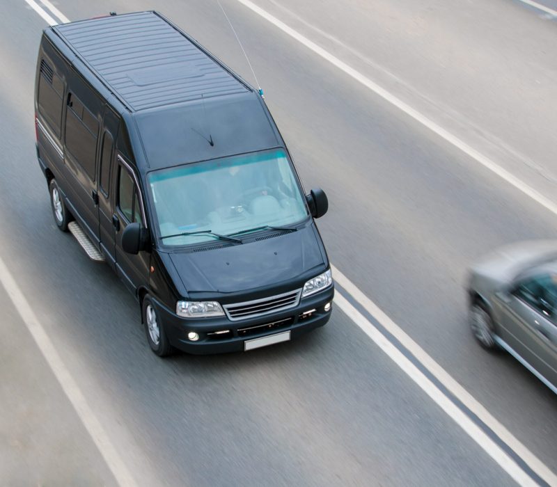Black cargo minibus driving on the freeway outside the city mid-plan landscape